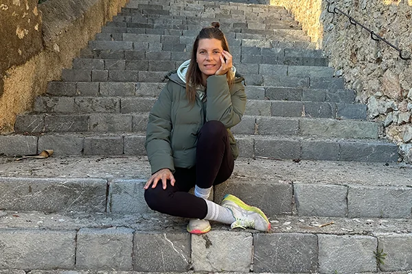 Melli Ketter sitzt auf einer Treppe und lächelt in die Kamera. Angekommen im Körper.